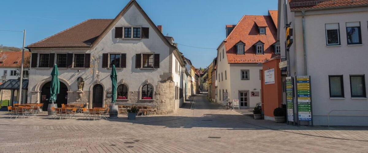 A cobblestone square with historic buildings, a fountain, and outdoor seating.
