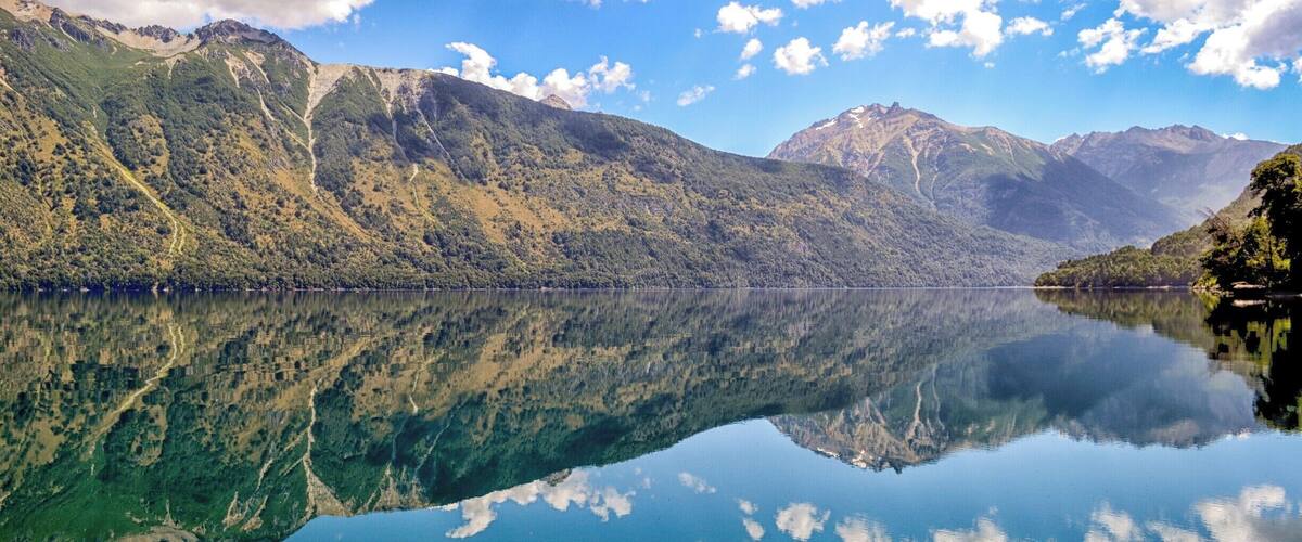 A calm lake with clear reflections of the surrounding mountains and sky.