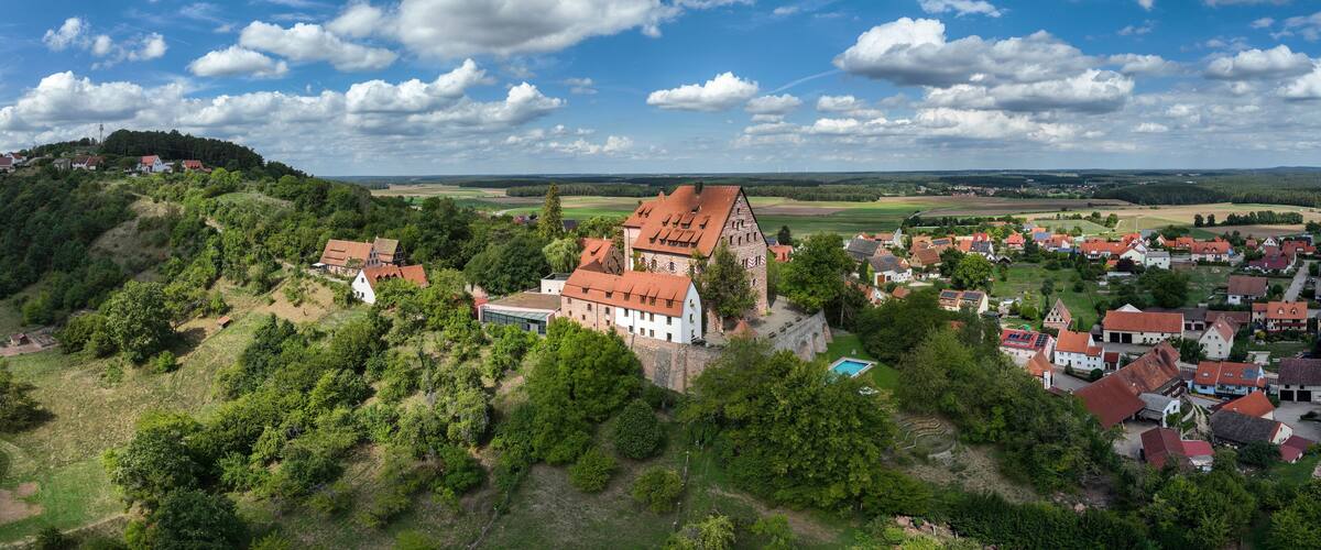 A historic town with a prominent castle on a hill, surrounded by lush greenery and a clear blue sky.
