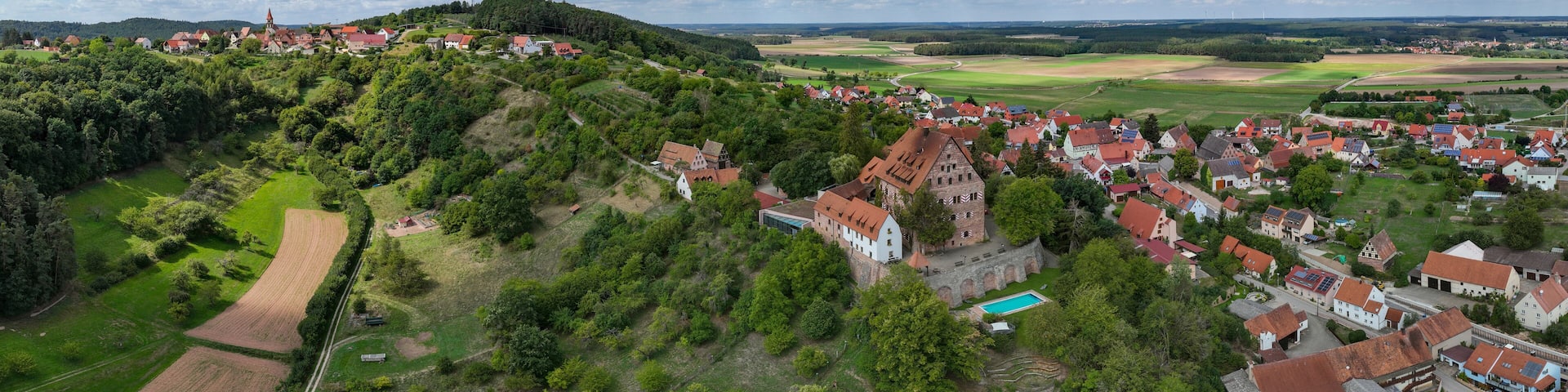 A village with red-roofed houses, a church, and a hill with trees.