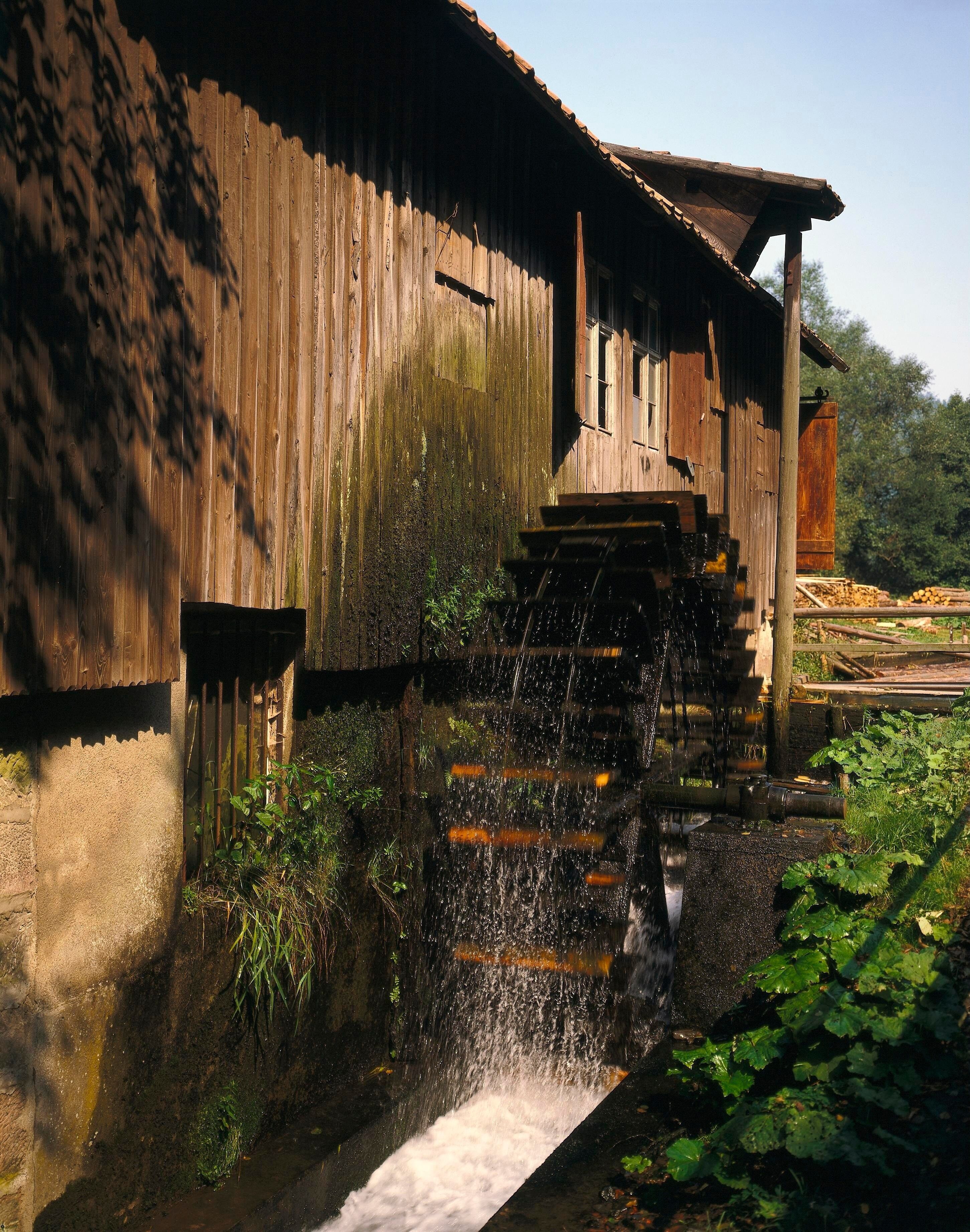 A wooden mill with a water wheel and a stream flowing from it.