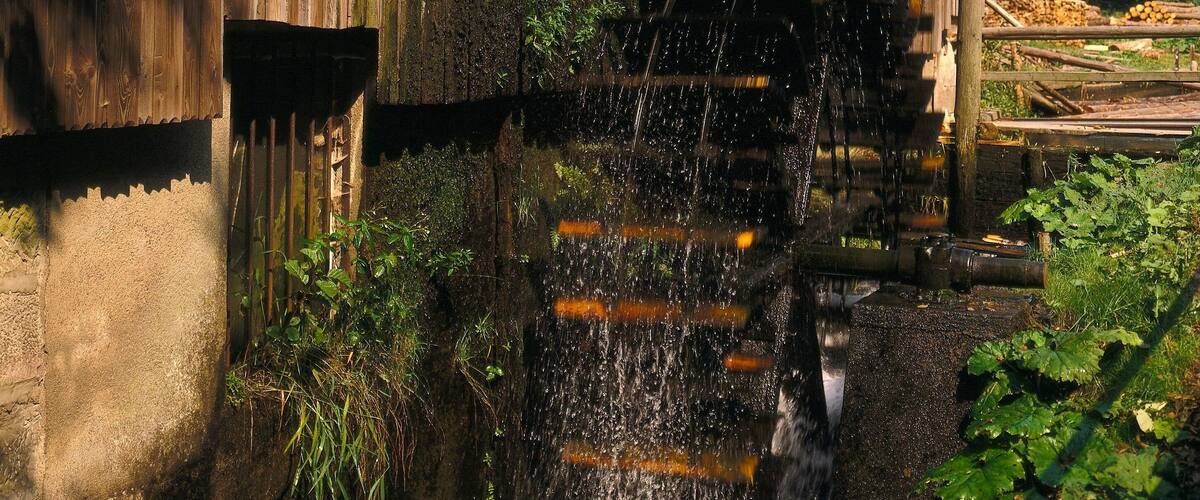 A wooden mill with a water wheel and a stream flowing from it.