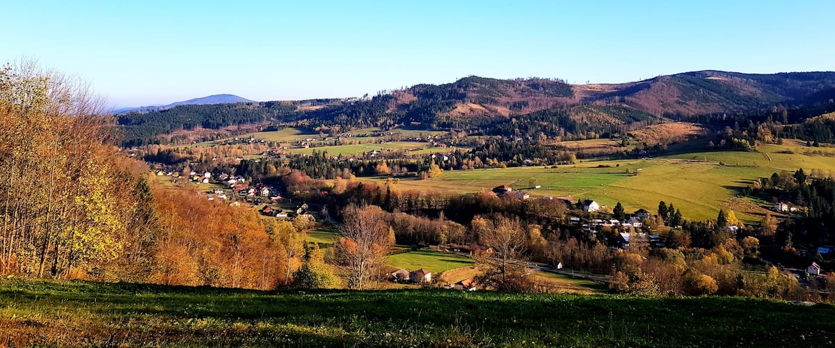 A rural landscape with rolling hills, scattered houses, and a clear blue sky.