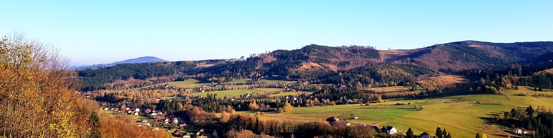 A rural landscape with rolling hills, scattered houses, and a clear blue sky.