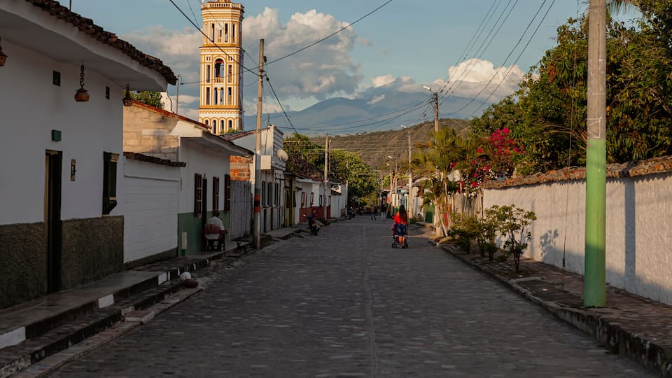 A cobblestone street lined with white buildings, a church tower, and a green utility pole.