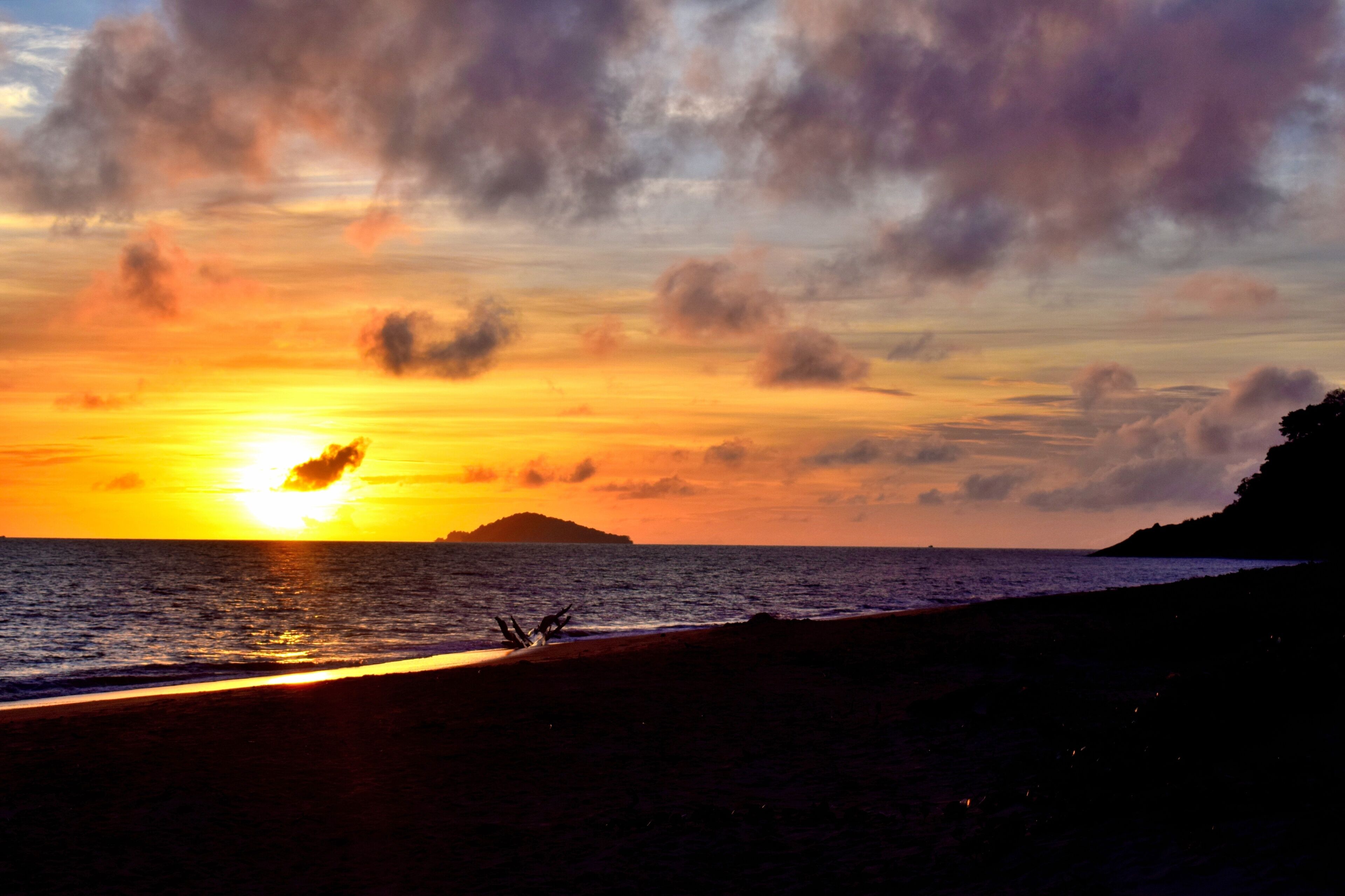 A sunset over a beach with a silhouette of a person and a distant island.