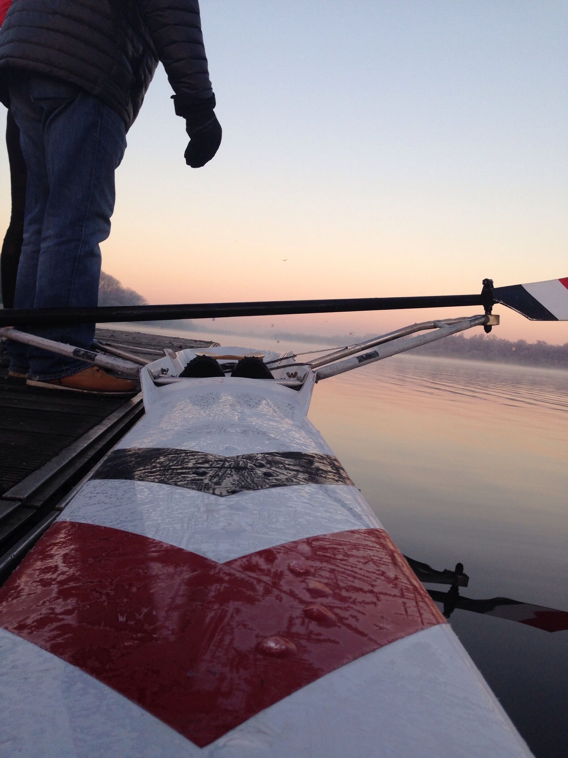 A boat with a red and white striped hull, a person standing on the deck, and calm water in the background.
