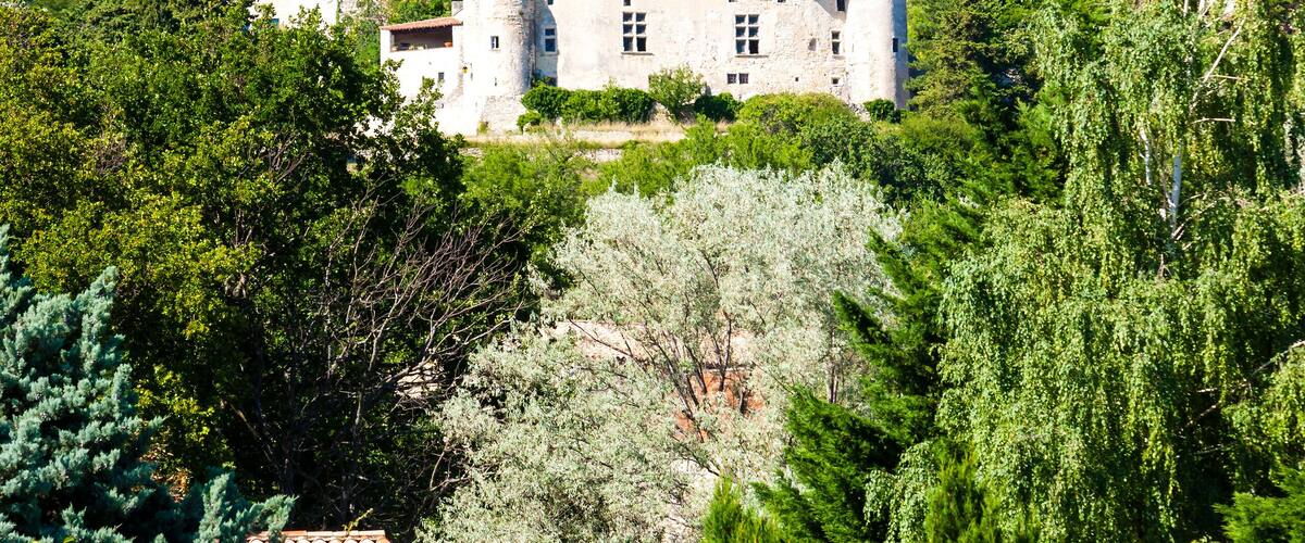 A historic stone building with multiple towers, surrounded by lush greenery and hills.