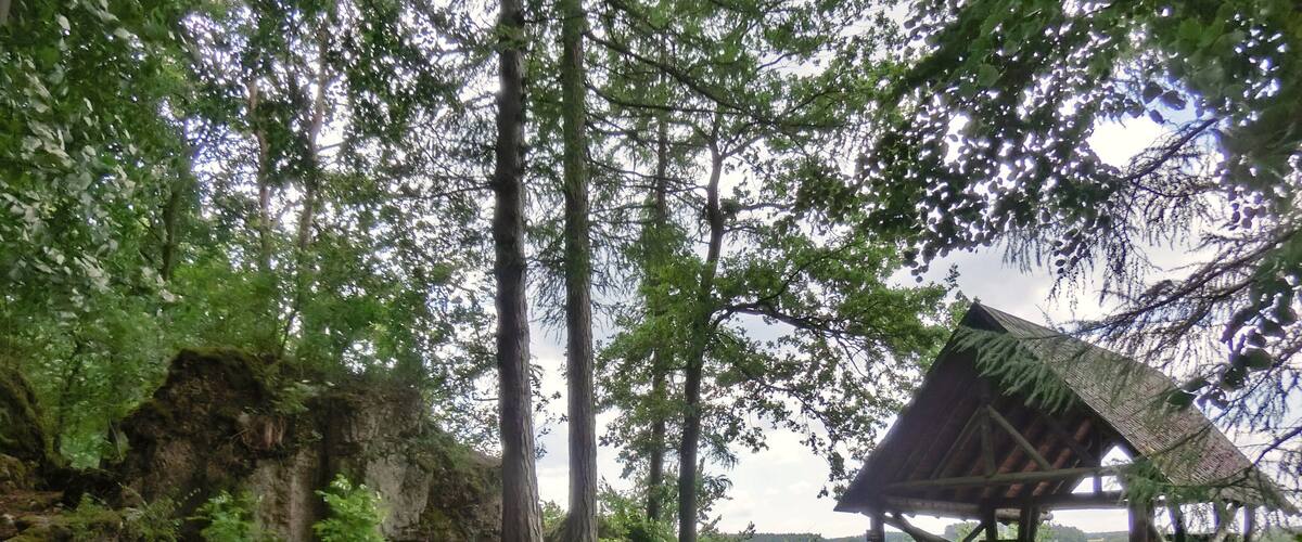 A rustic wooden structure in a forested area with a dirt path leading to it.