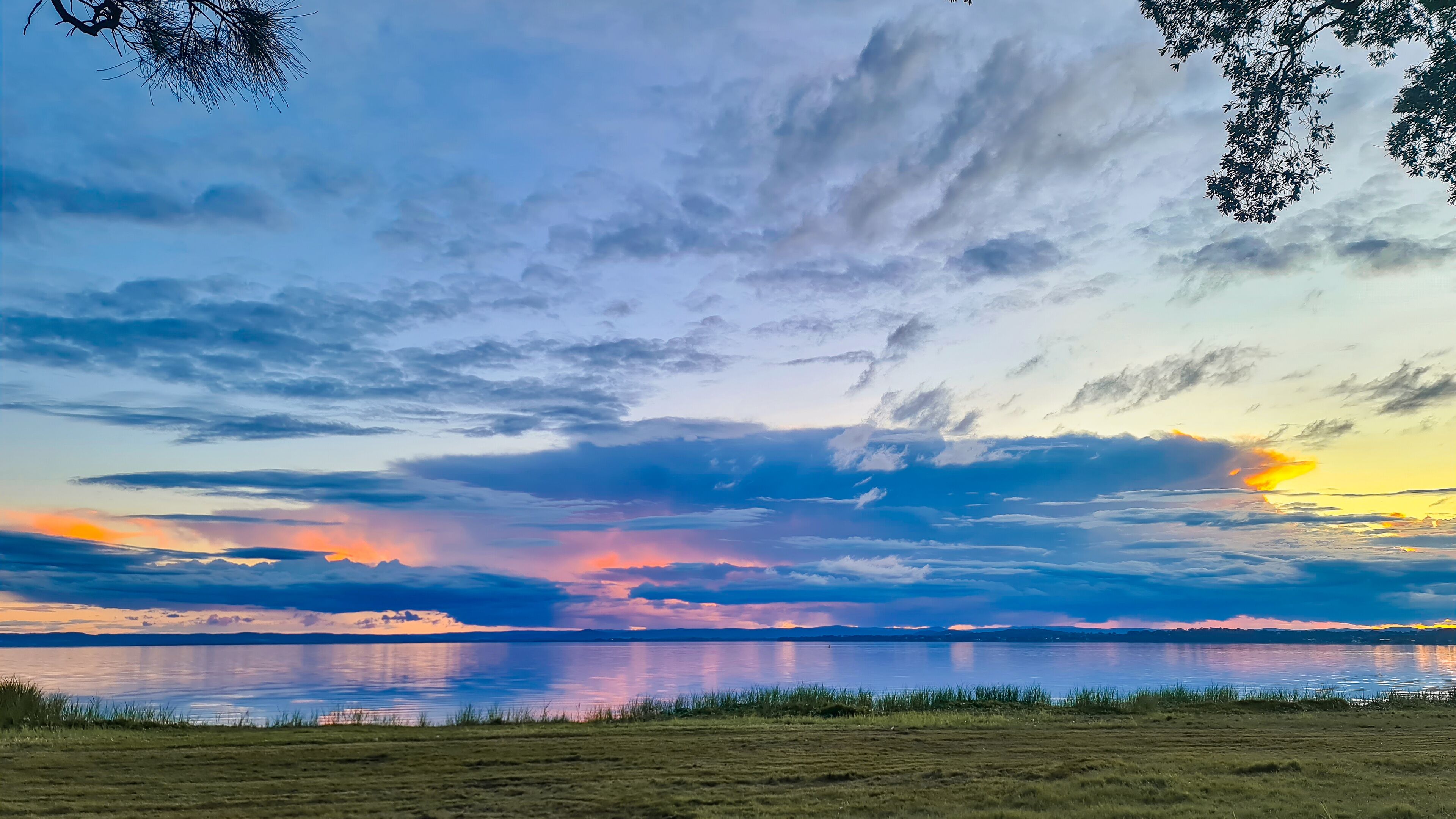 A sunset over a calm lake with a grassy foreground and scattered clouds.
