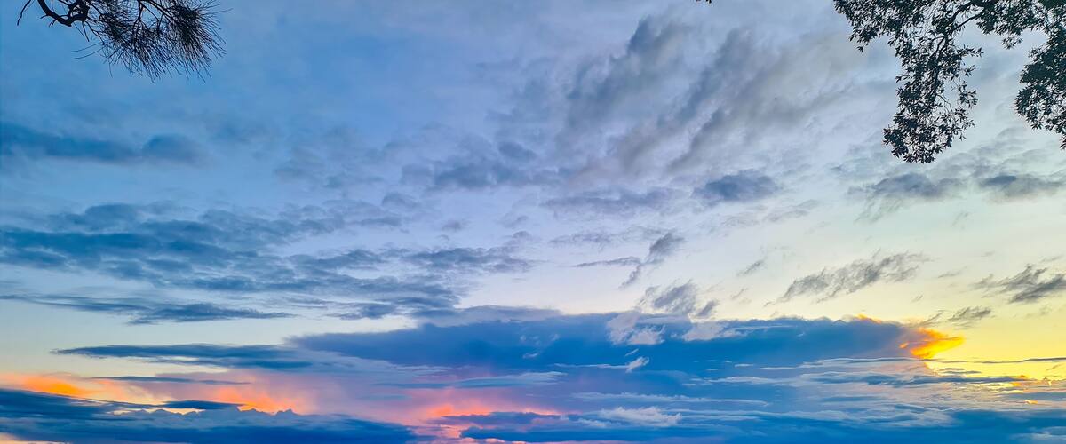 A sunset over a calm lake with a grassy foreground and scattered clouds.