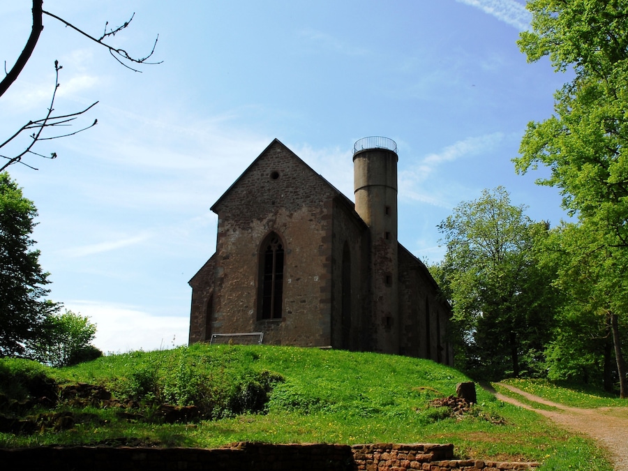 Une église dotée d’un clocher, entourée de verdure et bordée d’un sentier de terre.