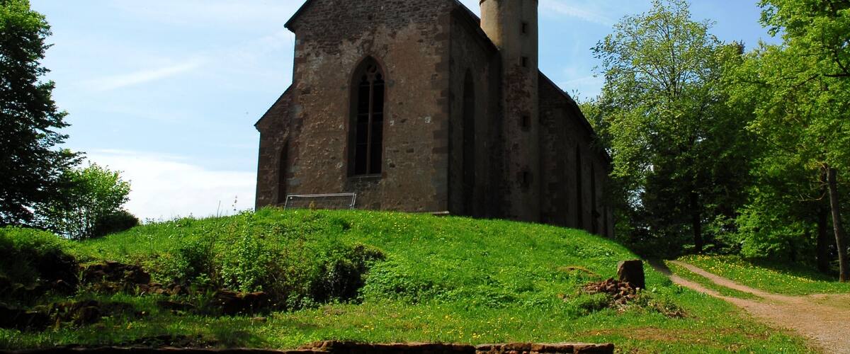 A church with a bell tower, surrounded by greenery and a dirt path.
