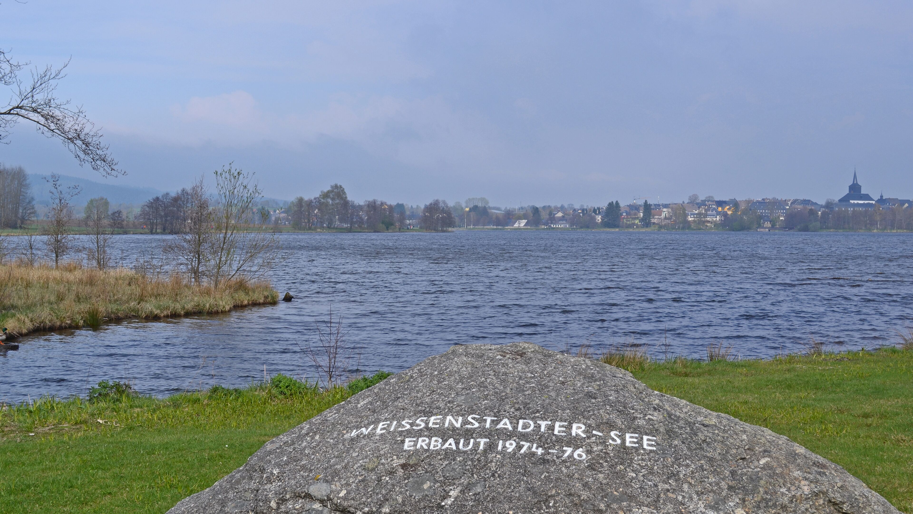 A lake with a rock inscribed with "WEISSENSTADTER ERBAUT 1974-76".