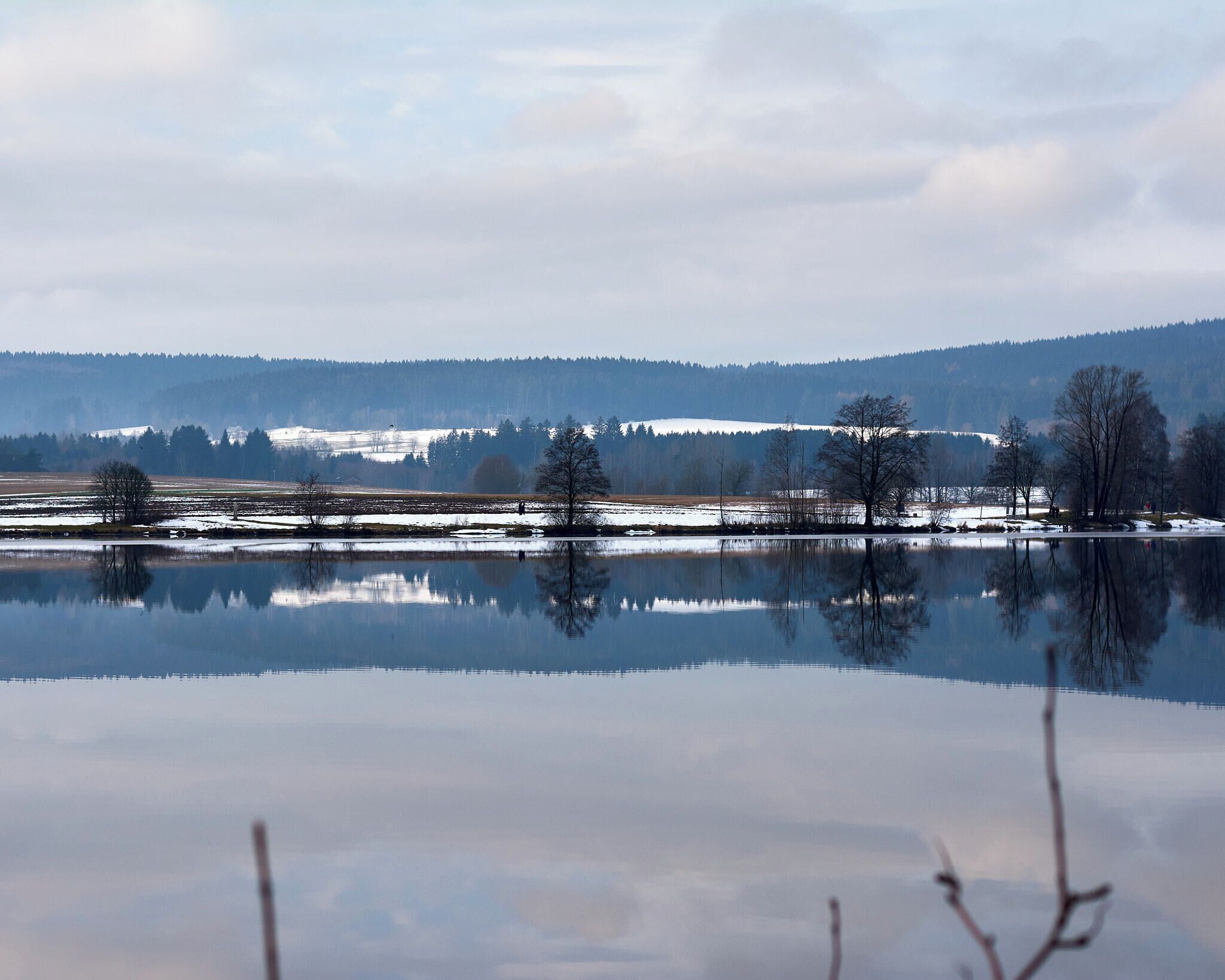 A calm lake reflecting trees and distant hills.