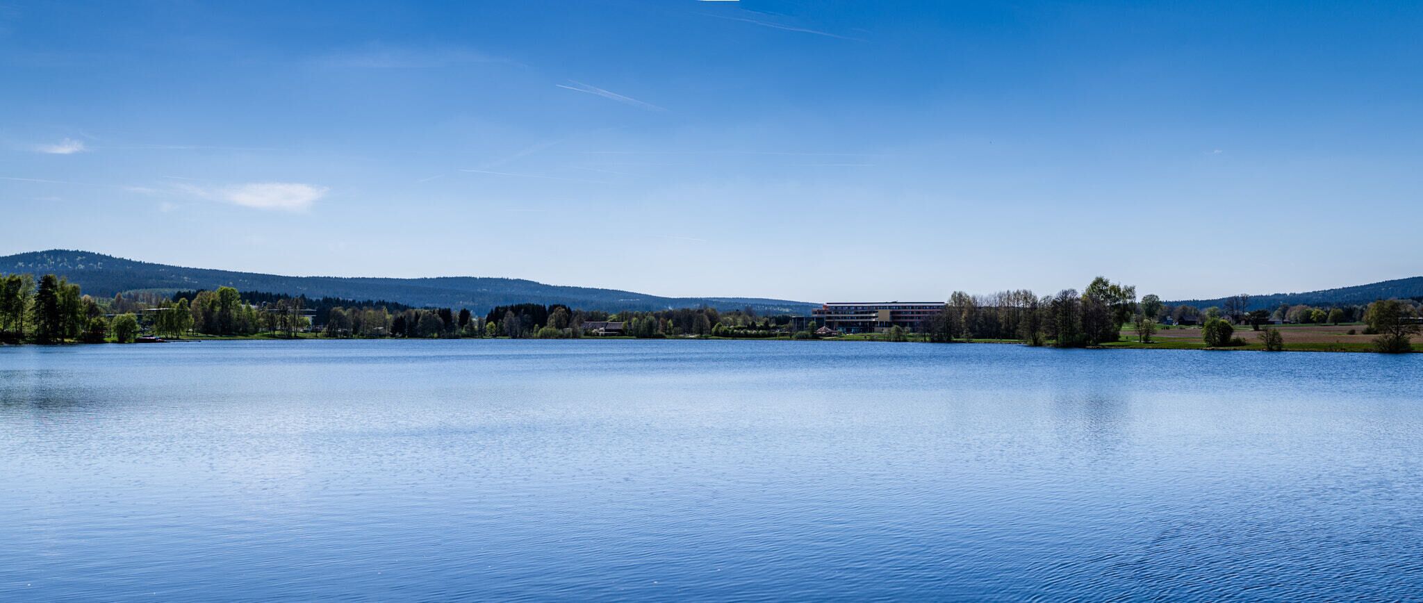 A calm lake with a clear sky, surrounded by trees and hills.