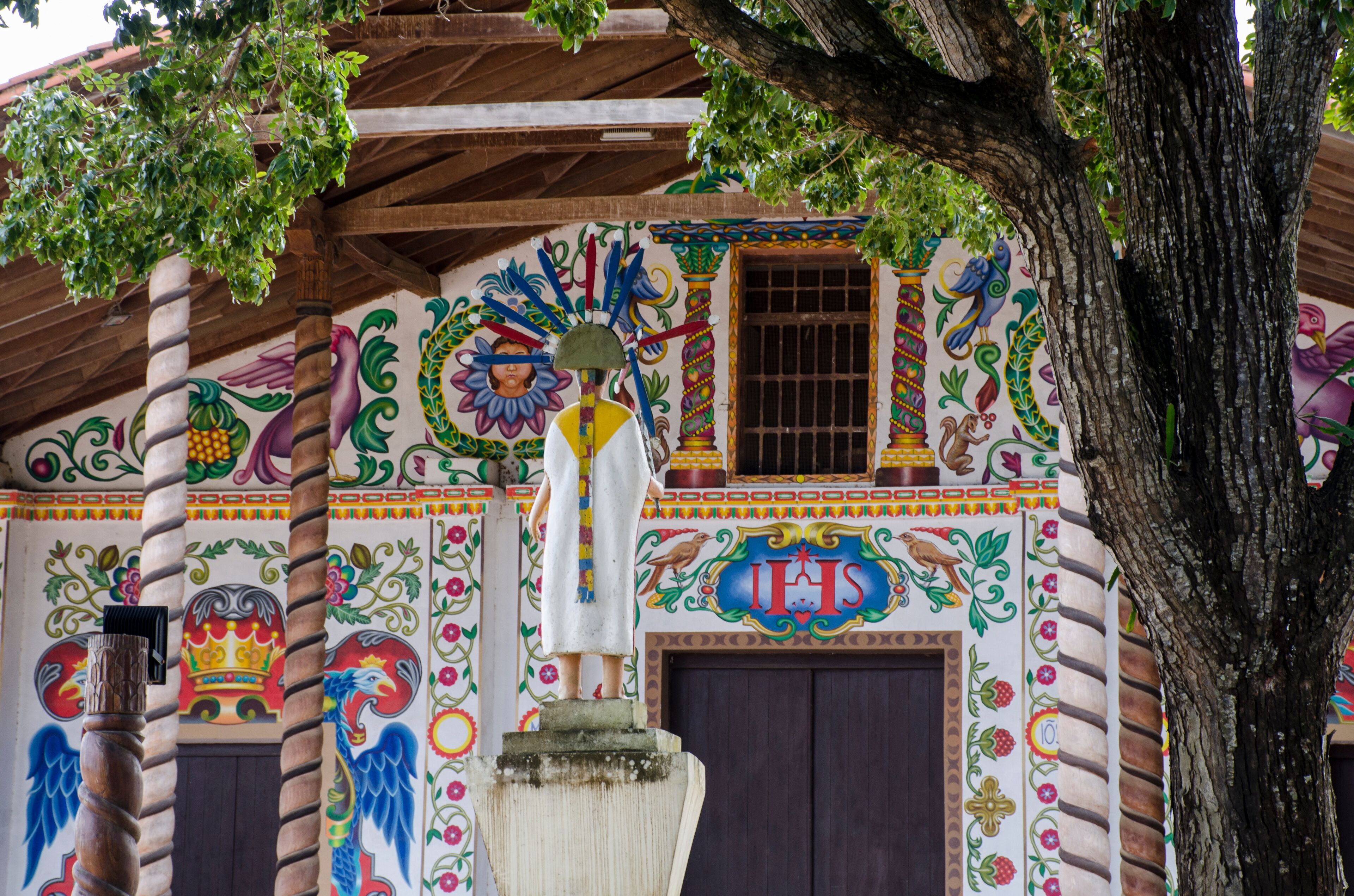 A colorful mural with a statue, a tree, and a building with a wooden roof.