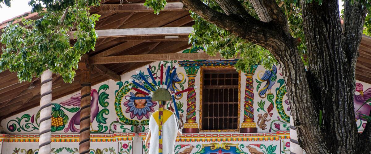 A colorful mural with a statue, a tree, and a building with a wooden roof.