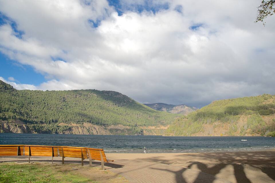 Un banc en bois donnant sur un lac, avec des montagnes en arrière-plan.