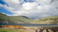Un banc en bois donnant sur un lac, avec des montagnes en arrière-plan.