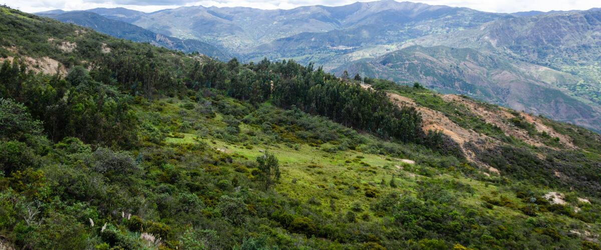 A mountainous landscape with dense green vegetation and distant mountain ranges under a cloudy sky.
