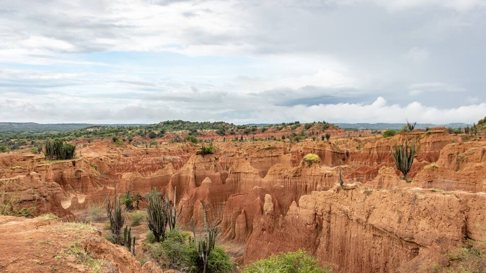 A rugged canyon landscape with red rock formations and sparse vegetation.