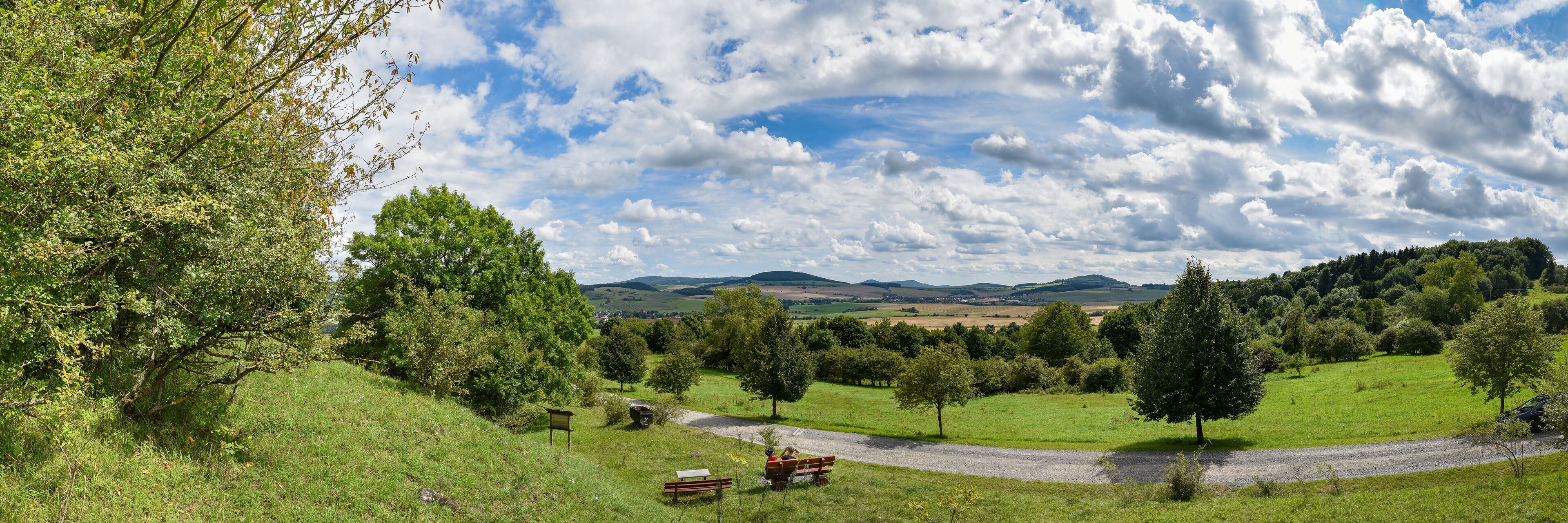 A rural landscape with rolling hills, a winding road, and scattered trees.