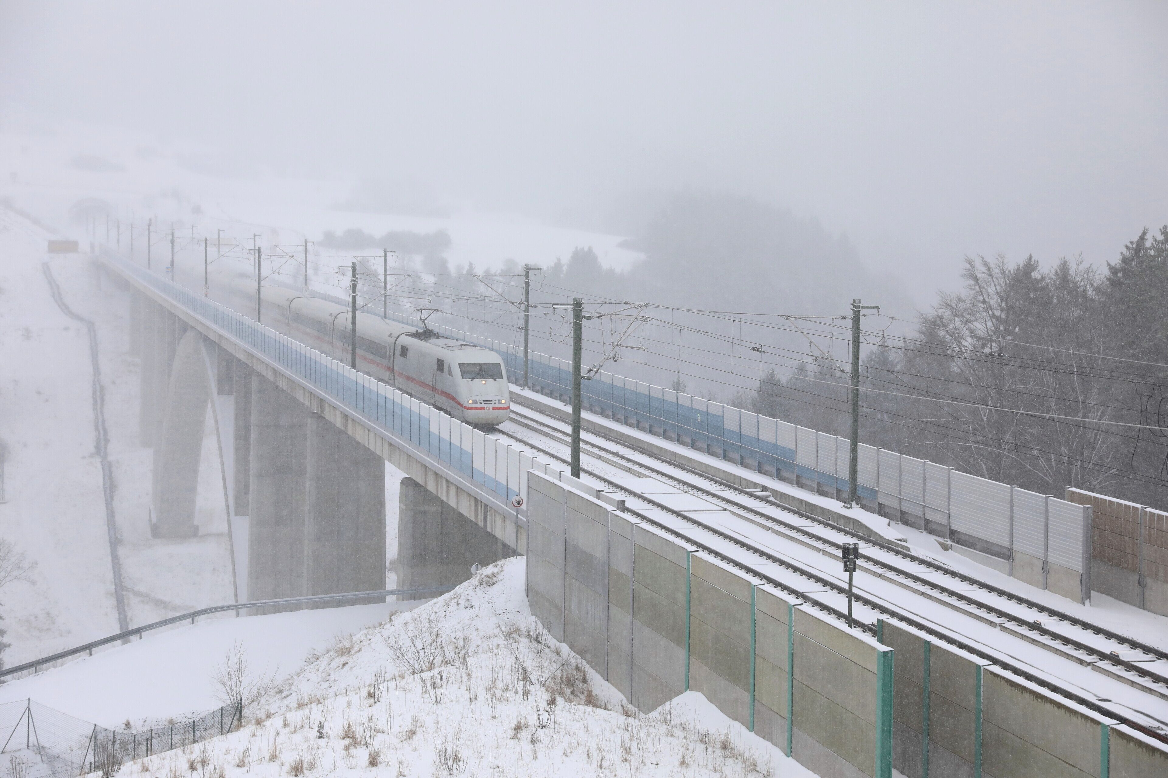 A train on a snow-covered bridge with a snowy landscape and power lines.