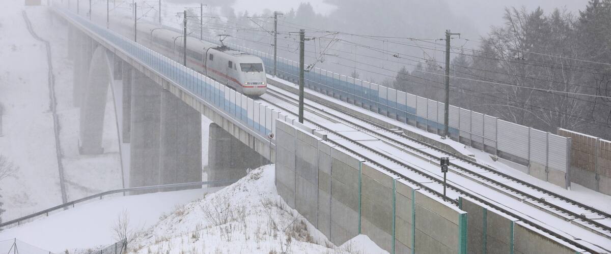 A train on a snow-covered bridge with a snowy landscape and power lines.