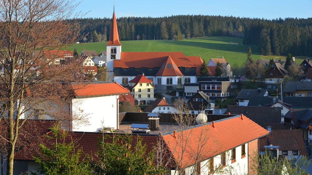 Eine Stadt mit einer markanten Kirche, Gebäuden mit roten Dächern und einem grünen Feld im Hintergrund.