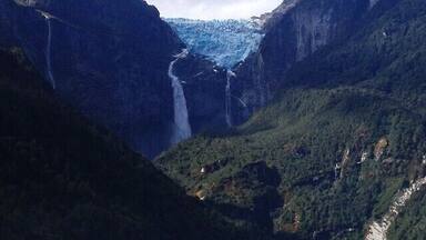 A glacier waterfall surrounded by steep, forested mountains.