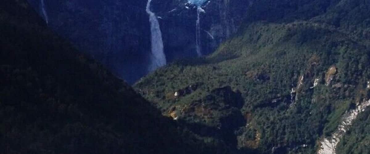 A glacier waterfall surrounded by steep, forested mountains.