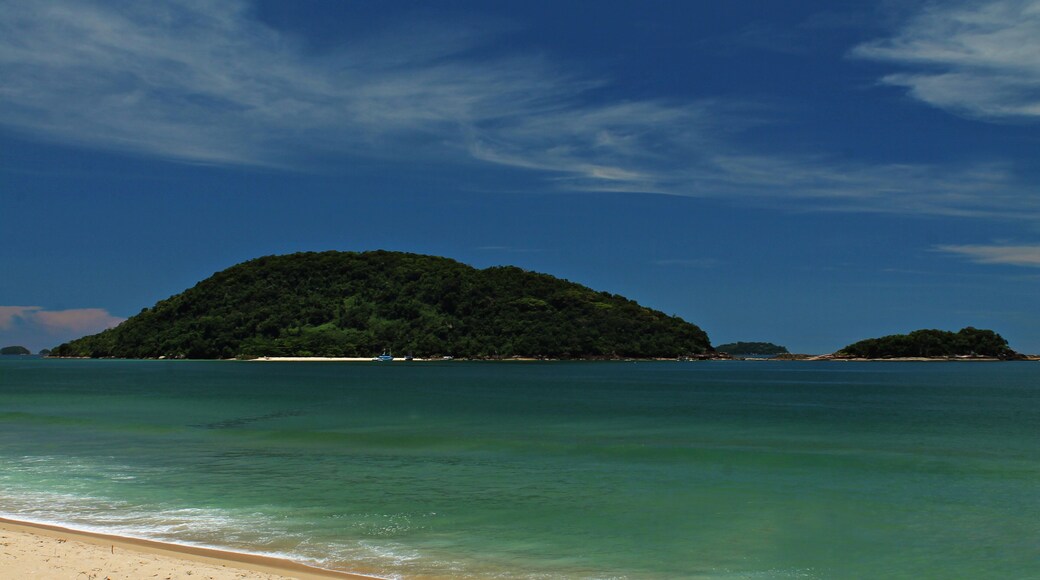 Praia do Prumirim, Ubatuba/SP, com a Ilha do Prumirim ao fundo, em dia ensolarado, águas cristalinas e montanhas cobertas por floresta tropical, destacando a natureza exuberante