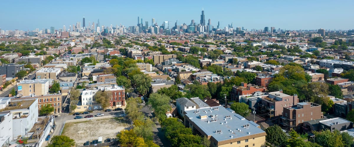 A cityscape with a dense urban area, a prominent skyscraper, and a clear blue sky.