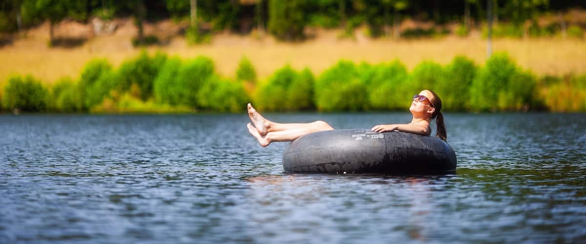 A person floating on a water tube in a lake surrounded by trees.