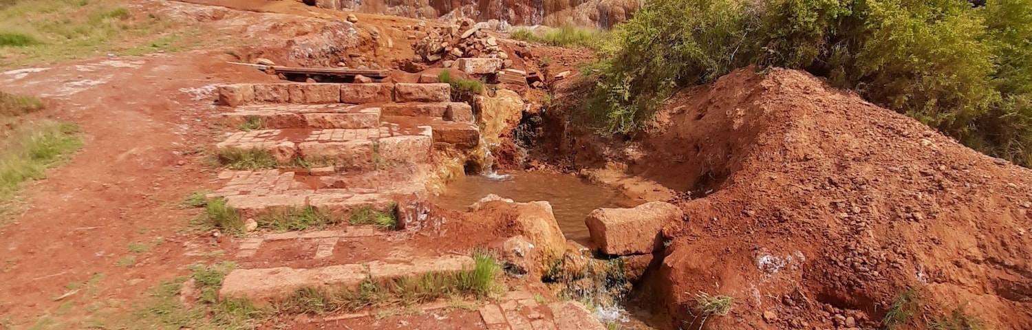 A rocky landscape with a small stream, a dirt path, and a hill in the background.