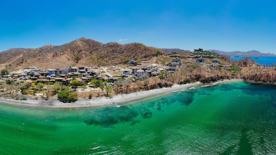 An aerial view of a coastal town with buildings on a hillside and a beach.