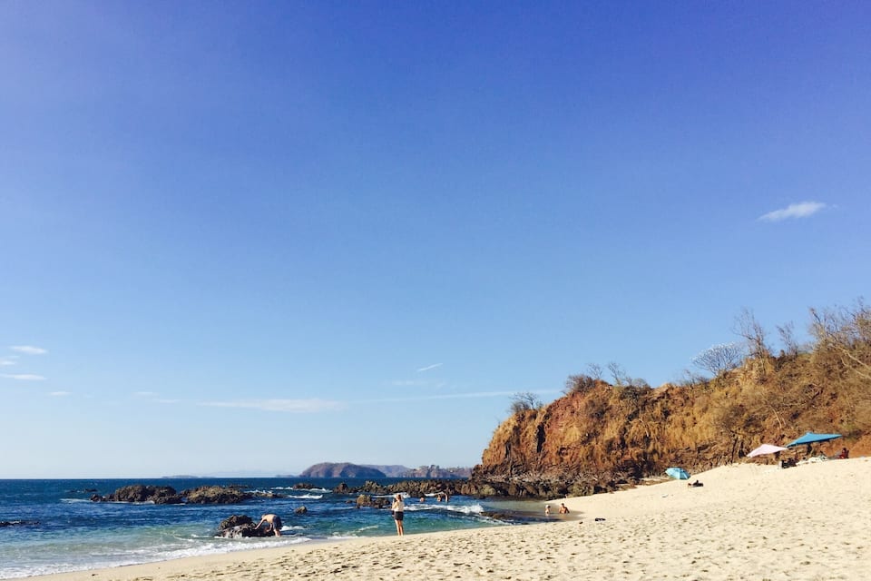 Une plage avec une eau d’un bleu limpide, des affleurements rocheux et une rive sablonneuse.