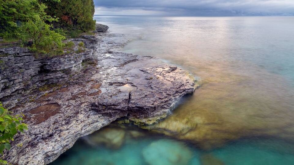 A rocky shoreline with clear water and a cloudy sky.