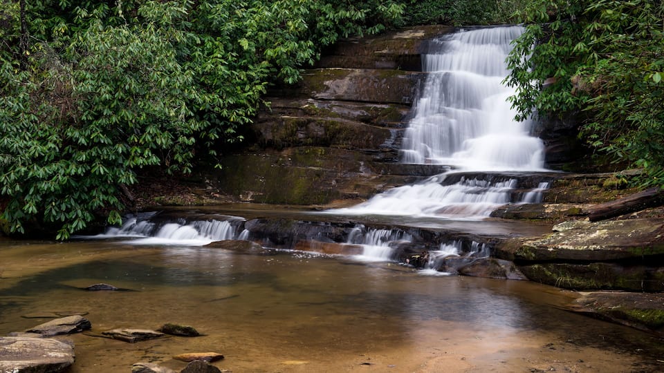 A multi-tiered waterfall surrounded by dense green foliage.