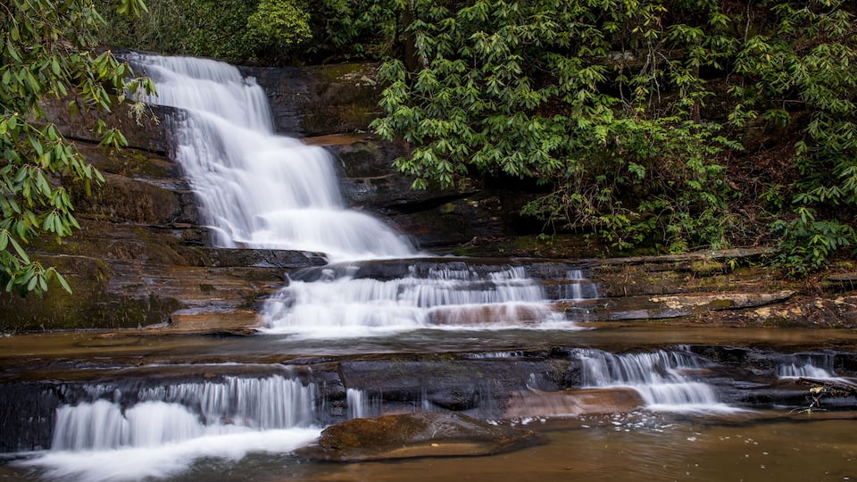 A multi-tiered waterfall surrounded by dense green foliage.