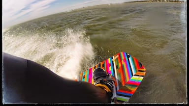 A person water skiing with a colorful board and a parasail in the background.