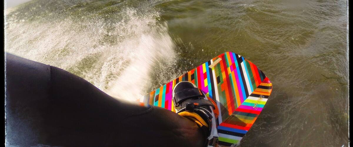 A person water skiing with a colorful board and a parasail in the background.