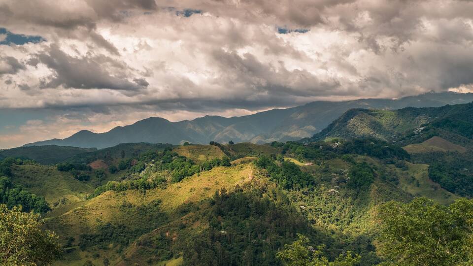 A mountainous landscape with dense forests and a cloudy sky.