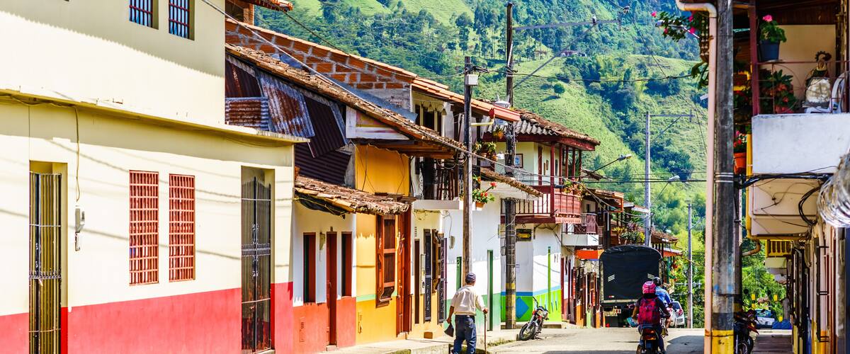 A street in a hilly town with colorful buildings, a man with a cane, and parked motorcycles.
