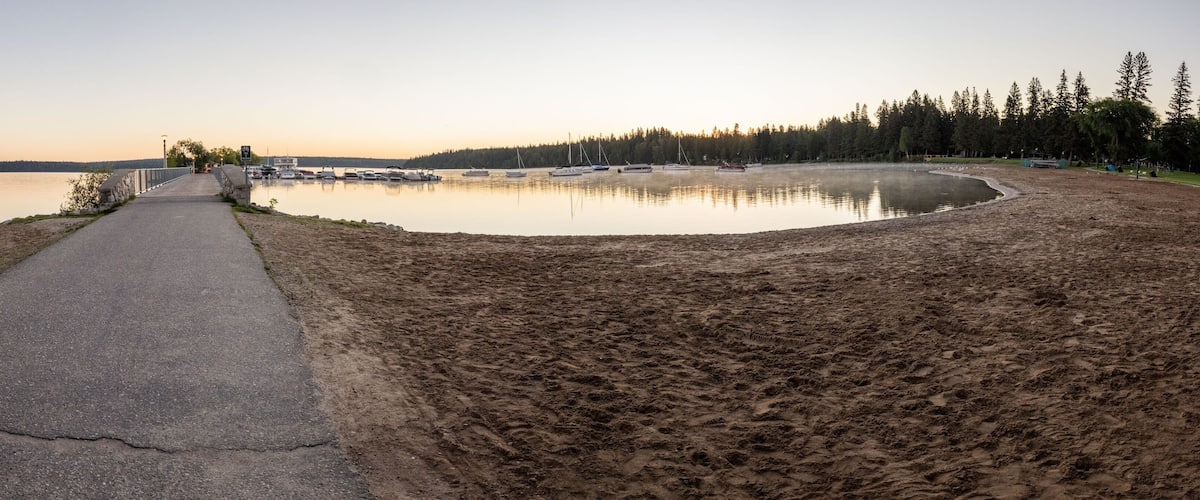 A paved path leading to a calm lake with boats docked, surrounded by a forested area.