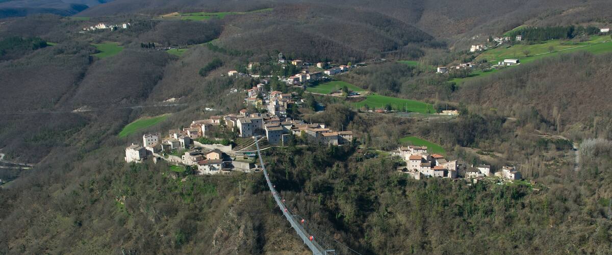 A village nestled in a valley with a suspension bridge connecting it to a higher area.