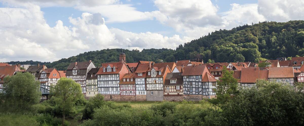 A town with traditional half-timbered houses, a hill with dense forest, and a partly cloudy sky.