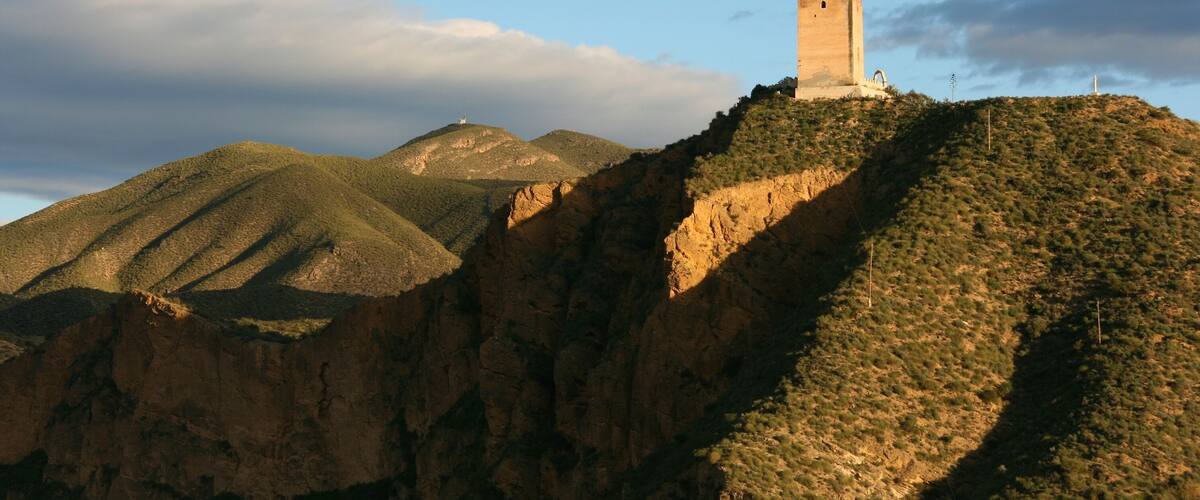A tower on a hill with surrounding hills and a clear sky.