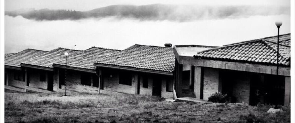 A row of buildings with tiled roofs, a grassy foreground, and a foggy mountain in the background.